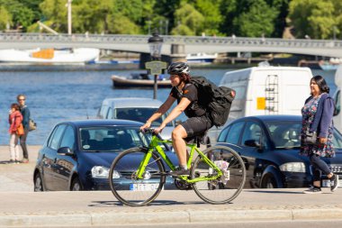 STOCKHOLM, İSVEÇ - 6 Temmuz 2017. Kasklı ve eşofmanlı bir kadın deniz kenarında bisiklet sürüyor. Açık hava eğlencesi. Avrupa 'ya bisiklet gezisi.