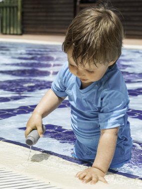 Yüzme havuzunda yıkanan tatlı bebek. Parlak mavi mayo giyen küçük çocuk havuzda oynuyor. Otelde tatil.. 