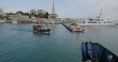 SOCHI, Rusya - 13 Mayıs 2021. Sochi limanından eski usul motorlu tekne kalkıyor. Hareket halindeki gemiden ana binaya bak.