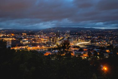 Norveç 'in başkenti Oslo' nun gece panoramik manzarası. Norveç 'in kara bulutlar altında yüzen başkenti. Ormanlarla çevrili, yanan binaları ve köprüleri olan İskandinav şehri..