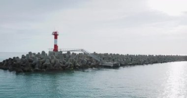 Hareket halindeki tekneden kırmızı beyaz çizgili deniz fenerine bakın. Çokgen beton parçalarından oluşan dalgalı su.