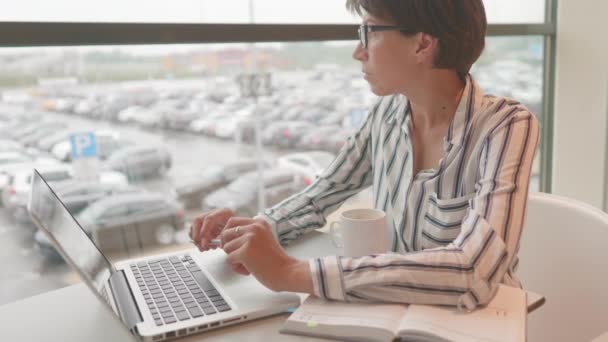 Серьезная деловая женщина в очках работает с ноутбуком и бумажным органайзером в коворкинг-центре. Рабочее место для фрилансеров в бизнес-центре. — стоковое видео