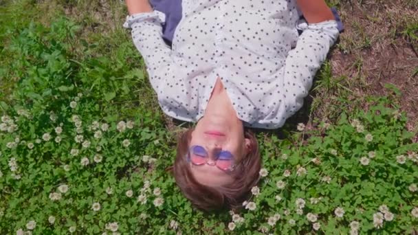 Bovenaanzicht op vrouw met kleurrijke zonnebril liggend op gazon in stedelijk park en geniet van bloemen. Zomer warmte in de stad. — Stockvideo