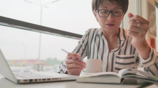 Seriös affärskvinna i glasögon arbetar med bärbar dator och pappersorganisatör i co-working center. Arbetsplats för frilansare i businesscenter. — Stockvideo