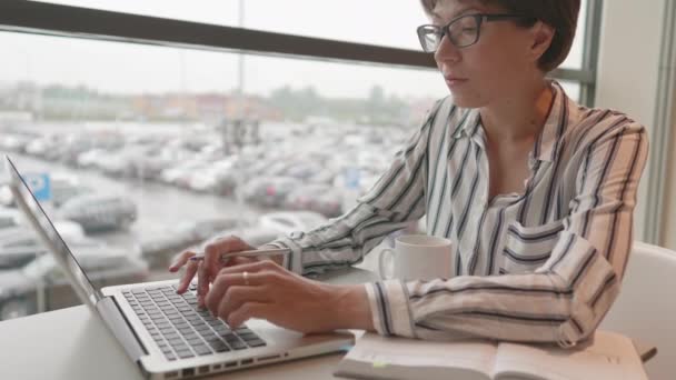 Serieuze zakenvrouw in bril werkt met laptop en papieren organisator in co-working center. Werkplek voor freelancers in bedrijvencentrum. — Stockvideo