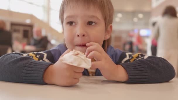 O miúdo come gelado no centro comercial. Criança bonito com saborosa sobremesa fria de cone de waffle com chantilly. — Vídeo de Stock