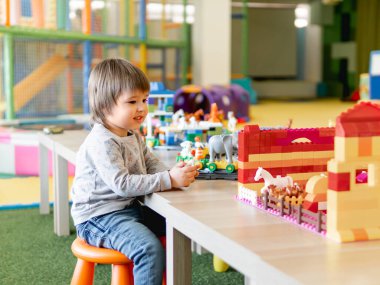 Bebek renkli oyuncak bloklarıyla oynuyor. Küçük çocuk oyuncakçıdan figürlere bakıyor. Anaokulu ya da kreş. Çocuklar için kapalı alan aktivitesi.