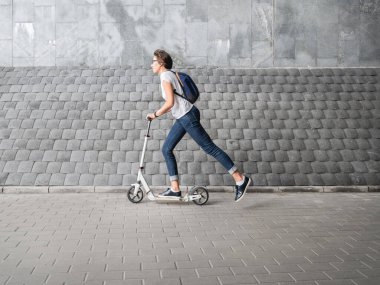 Kadınlar scooter 'a biner. Kotlu ve spor ayakkabılı bir kadın gri kiremitli arka planda hızlı hareket eder. Sağlıklı bir yaşam tarzı. Çevre dostu şehir ulaşımı.