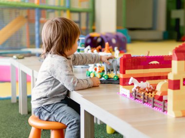 Bebek renkli oyuncak bloklarıyla oynuyor. Küçük çocuk oyuncakçıdan figürlere bakıyor. Anaokulu ya da kreş. Çocuklar için kapalı alan aktivitesi.