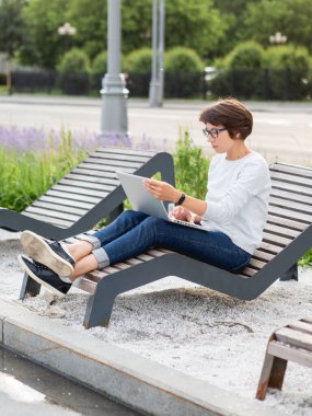 Kadın dizüstü bilgisayarla şehir parkındaki bankta oturuyor. İşyerinde serbest çalışan biri. Öğrenci, dışarıdan uzaktan öğreniyor. Modern yaşam tarzı.