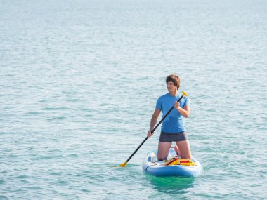 Yakışıklı kürekçi seni. Sporcu dizlerinin üzerinde ayakta kürek çekiyor. Sup sörfü. Aktif yaşam tarzı. Açık hava eğlencesi. Deniz kenarında tatil..