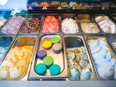 Renkli dondurma ve hamur işleriyle dolu metal kaplar. Şekerci dükkanının vitrininde farklı malzemelerle doldurulmuş soğuk tatlılar..