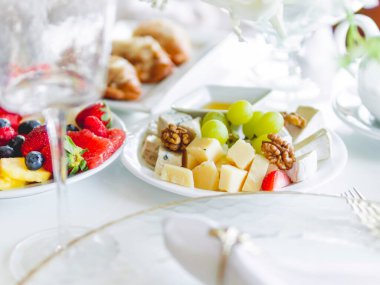 Ziyafet için servis edilen masa. Meyve ve aperatifli tabaklar, şeffaf modern şarap bardakları ve beyaz masa örtüsü üzerindeki çatal bıçak takımı..