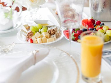 Ziyafet için servis edilen masa. Meyve ve aperatifli tabaklar, şeffaf modern şarap bardakları ve beyaz masa örtüsü üzerindeki çatal bıçak takımı..
