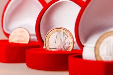 Red gift boxes with one euro, ten roubles and one cent coins. Focus on euro coin, the official currency of the eurozone (European Union). clipart