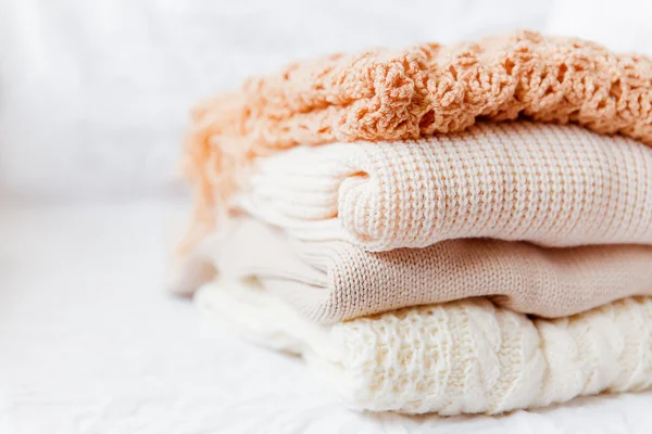 Pilha de roupas de lã bege em um fundo branco. Camisolas de malha quentes e lenços são dobrados em um montão — Fotografia de Stock