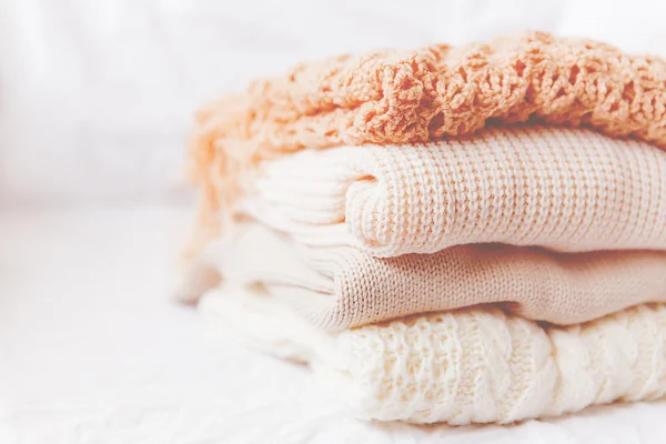 Pile of beige woolen clothes on a white background. Warm knitted sweaters and scarfs are folded in one heap. Imitation of Instagram style tone. — Stock Photo, Image