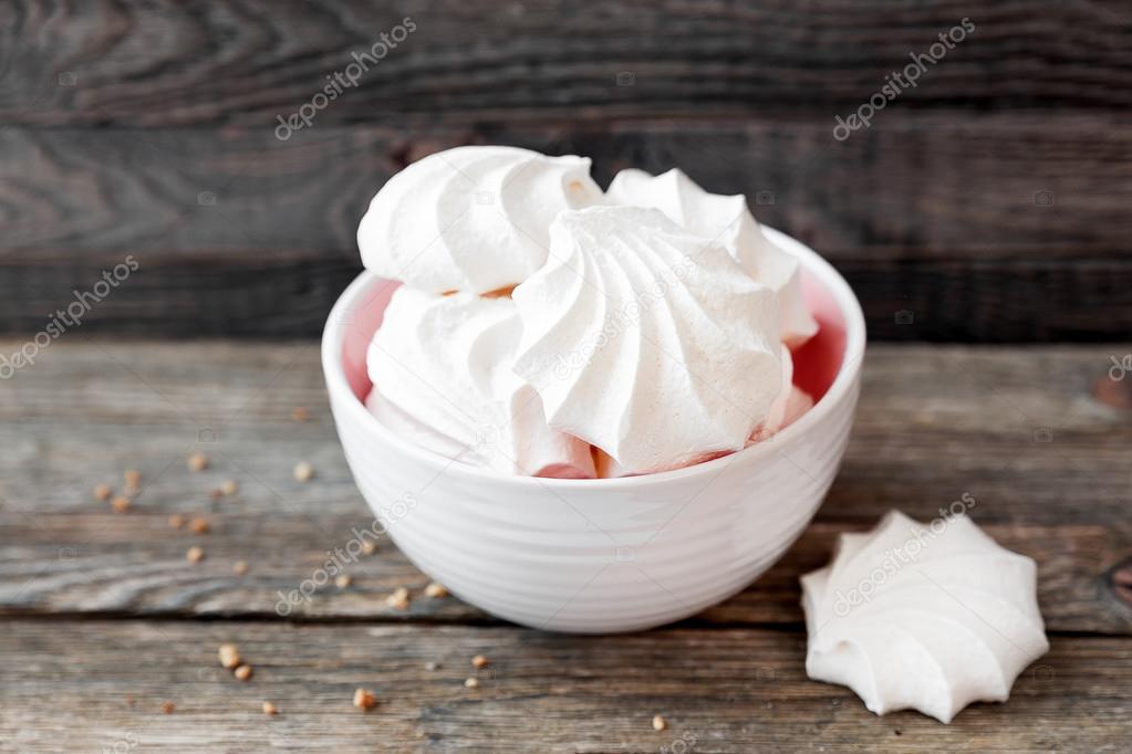Some tasty meringues lie in a white bowl on a wooden background.
