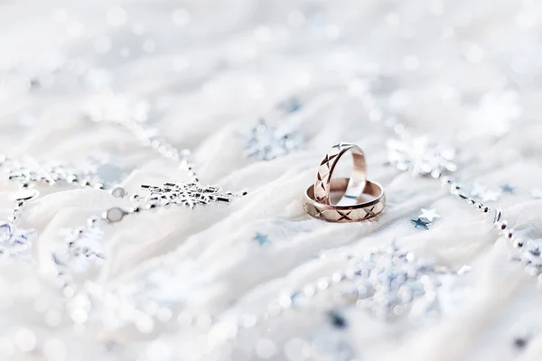 Trouwringen op witte vakantie achtergrond met mousserende zilveren sneeuwvlokken, kerstversiering. Symbool van de bruiloft in de winter. — Stockfoto