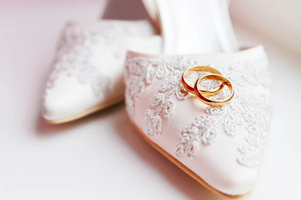 Gouden trouwringen op kant zijde stof schoenen. — Stockfoto