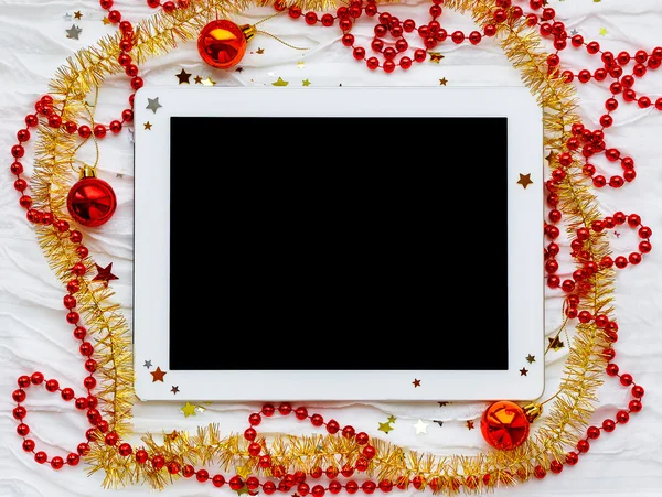 Tableta sobre fondo de vacaciones de invierno. Adornos navideños - oropel rojo y amarillo, destellos de estrellas, abalorios . — Foto de Stock