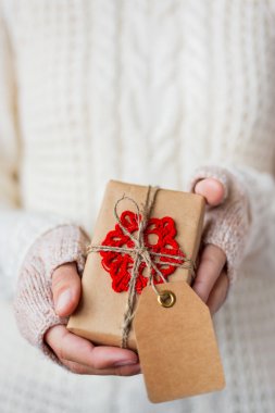 Woman in white knitted sweater and mitts holding a present.