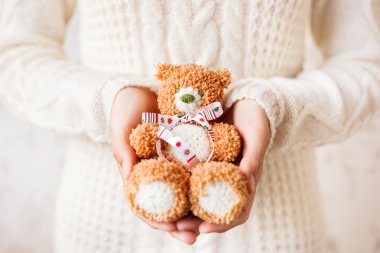 Woman in white knitted sweater holding toy bear with christmas ribbon. Hand made crocheted little bear is a present for kid