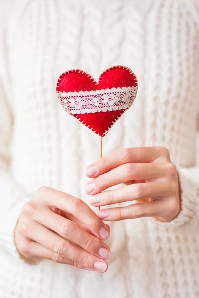 Femme en pull tricoté tenant un coeur rouge feutre avec une ligne de dentelle. Symbole rouge vif de l'amour. Saint-Valentin fond . — Photo