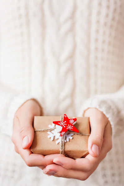 Женщина в вязаном свитере с подарком. Подарок упакован в бумагу с белым войлоком снежинки и красной звездой . — стоковое фото