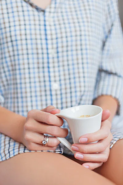 Vrouw in shirt zit op bed met een kop met warme koffie. — Stockfoto