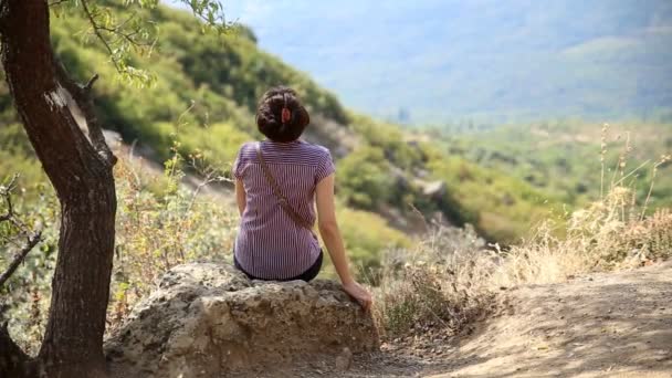 La chica se está estirando mientras está sentada en una piedra. Vista desde la montaña. Crimea . — Vídeos de Stock