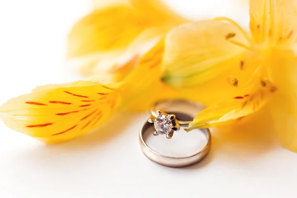 Pair of wedding and engagement rings with yellow Alstroemeriaflower. Natural background with symbol of love and marriage. Close up. — Stock Photo, Image