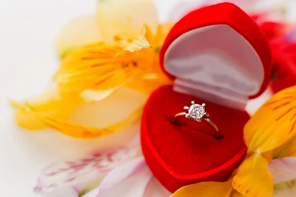 Verlobungsring in roter Geschenkbox auf einem Haufen Blütenblätter. Symbol für Liebe und Ehe. — Stockfoto