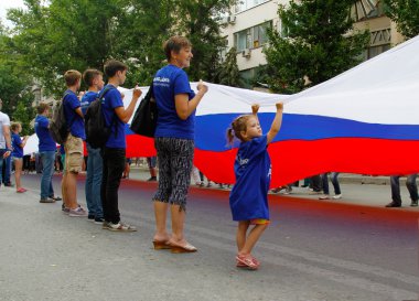 Volgograd, Russia - June 12, 2015: Little girl together with other activists hold a large Russian flag on the Independence day of Russia in Volgograd clipart