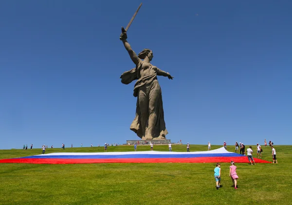Volgograd, Rusland - 12 juni 2013: Jongen en meisje gaan te hulp ontplooiing een grote Russische vlag in dag van Rusland aan de voet van het monument van moederland verzoekt Mamaev heuvel in Volgograd activisten — Stockfoto