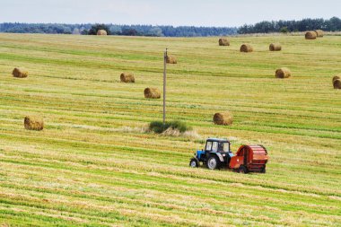 Traktör haystacks olan bir alana arka planda yuvarlak balya çeker