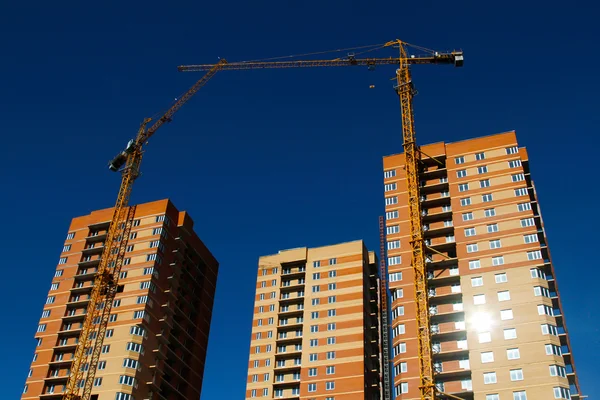 Bouw van bakstenen huizen met kranen over blauwe hemel — Stockfoto