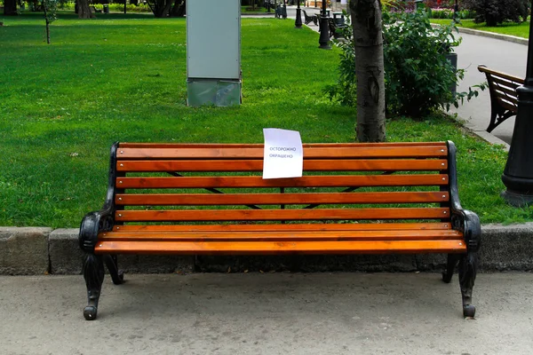 Eine frisch gestrichene Bank im Park mit einem Warnschild (übersetzt aus dem Russischen "Vorsicht. Nasse Farbe") — Stockfoto