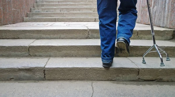 Destekli bastonlu yaşlı adam merdivenleri çıkıyor.