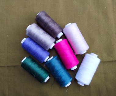 Yeşil, mavi, pembe ve beyaz gibi çeşitli renklerde iplik makaraları yeşil bir yüzeye dizilmiştir.