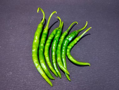 Altı canlı yeşil biber dikey olarak koyu dokulu bir yüzeye dizilir..