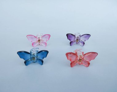 Beyaz yüzeye dizilmiş dört renkli yarı saydam kelebek saç tokası..