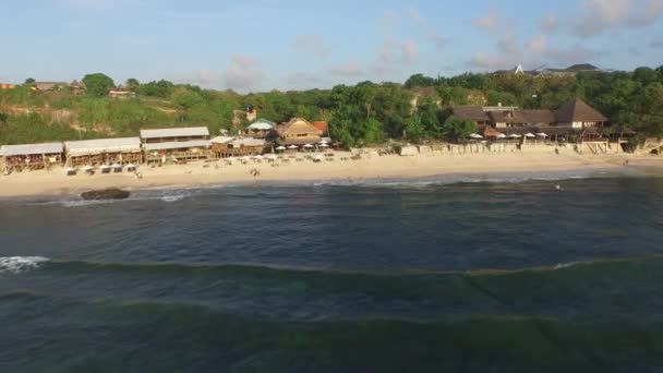 Volare sulle onde verso i ristoranti sul mare sulla spiaggia di Balangan, Bali, Indonesia (video aereo ) — Video Stock