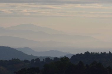 Dağların siluetleriyle kaplı bir manzara Sabah sisli ve bulutlu