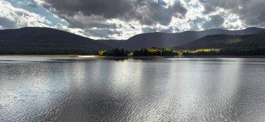 Catskill Dağları 'ndaki Ashokan Barajı' nın yaz manzarası. Güneş ışığı dramatik bulutları delip geçiyor, dalgalı sularda yansıyor ve uzaktaki dağ siluetleriyle. Appalachian Dağlarında manzaralı bir Hudson Vadisi manzarası.