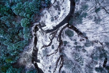 New York 'taki Catskill Dağları' ndaki karlı bir ormanı kesen dolambaçlı bir nehrin yukarıdan aşağıya insansız hava aracı görüntüsü. Kış manzarası, karla kaplı ağaçlar, akan karanlık sular ve yukarıdan görülen doğal desenler. Sahne vahşi arka planı.