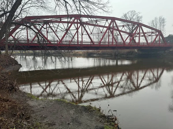 New York Hudson Vadisi 'nde sakin bir sabahta kırmızı çelik kiriş köprüsü nehir suyuna yansıdı. Atmosferik manzara çıplak ağaçlar, yumuşak ışık ve durgun su ile doğal manzarayı tarihi altyapı ile harmanlıyor..