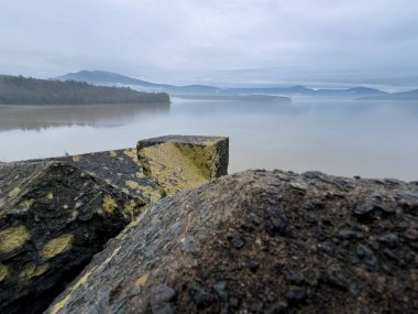 Ashokan Barajı 'nın taş blokları, New York' un Ulster ilçesinde sisli ve bulutlu bir günde, Catskill Dağları 'nın uzak sırtlarında siste sürüklenen sis yüzünden durgun sulara karışır..