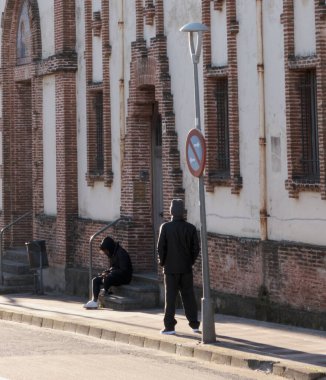 Sokak basamaklarında oturan bir kadın akıllı telefonunun ekranına bakıyor. Arkadan bir adam izliyor gibi..