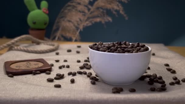 咖啡豆散落在白色的杯子里，落在木制桌子上慢动作 — 图库视频影像